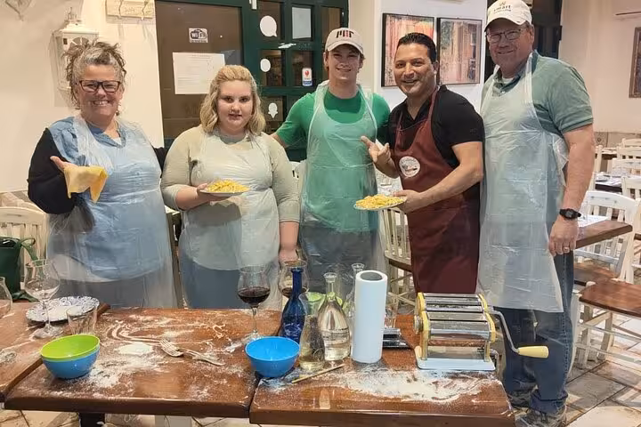 Happy group displaying gluten-free pasta they made in a Rome cooking class, featuring pasta machines and flour-covered tables.