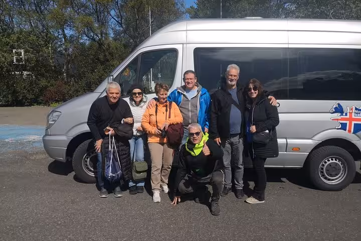Group of travelers smiling by a shuttle van in Akureyri, ready for the Godafoss Express round trip with multiple drop-off choices.
