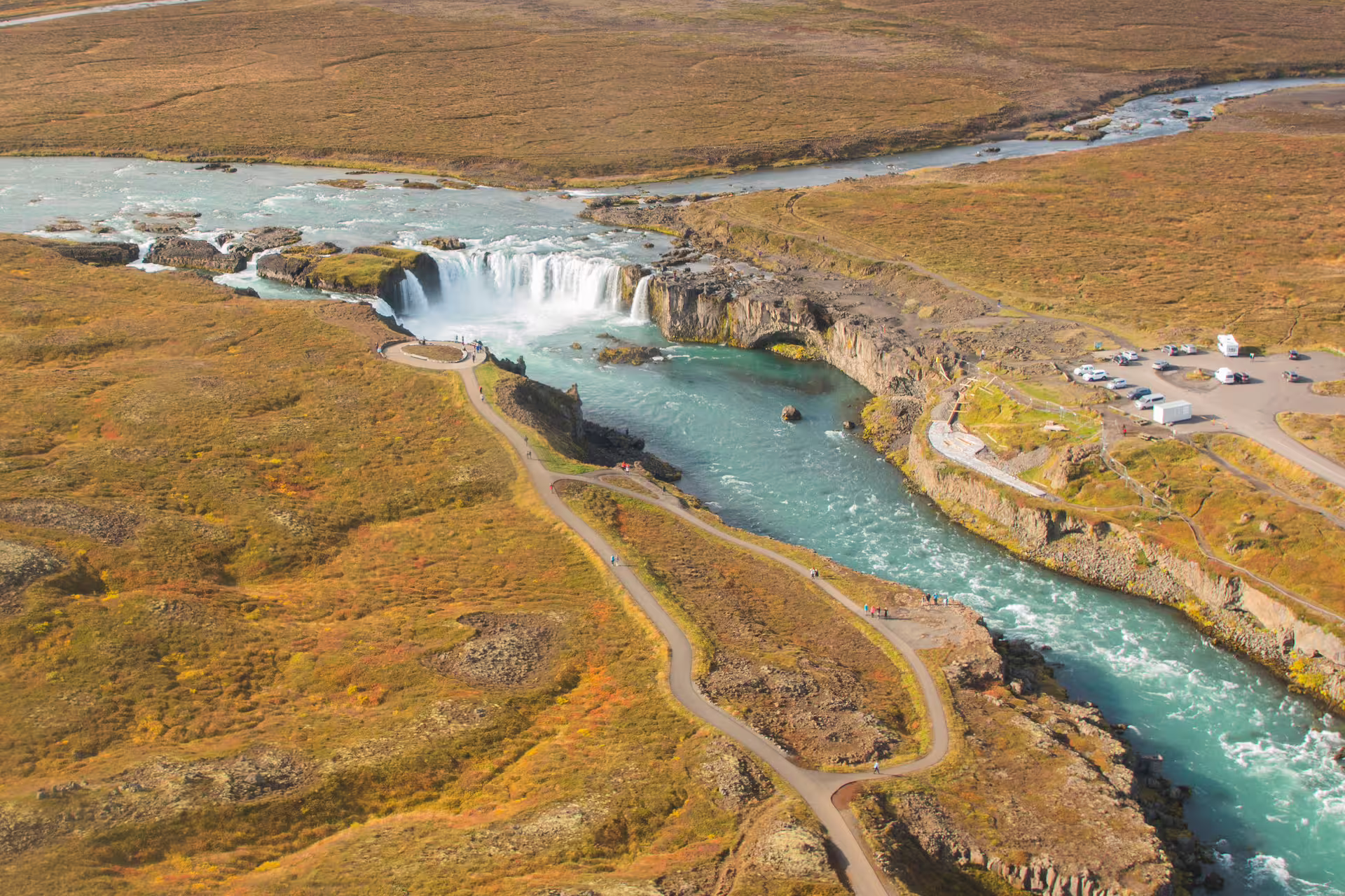 Aerial view of Godafoss waterfall with turquoise river canyon and walking paths in Iceland