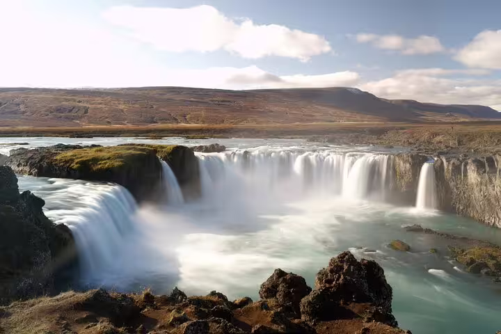 Godafoss waterfall cascading over wide rocky ledge with turquoise pool, rolling hills in background, Iceland