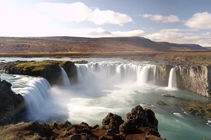 Godafoss waterfall cascading into turquoise pool surrounded by rocky cliffs and rolling hills in Iceland