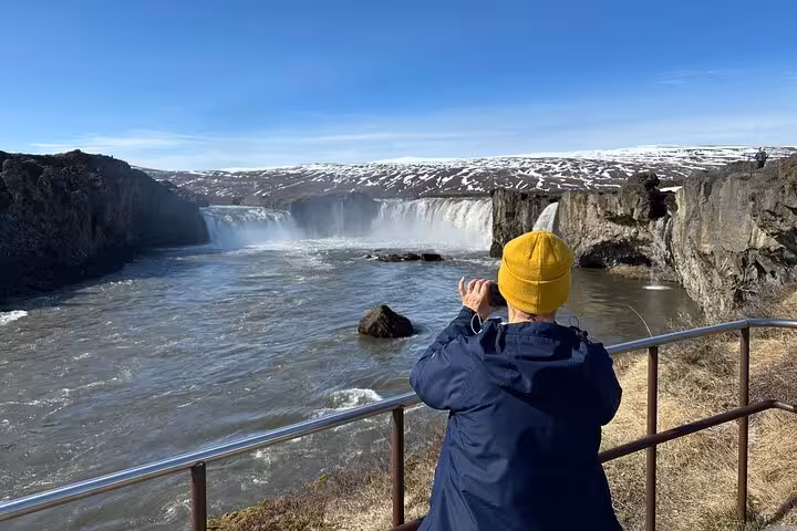Visitor capturing the stunning Godafoss Waterfall on a sunny day tour from Akureyri, Iceland.