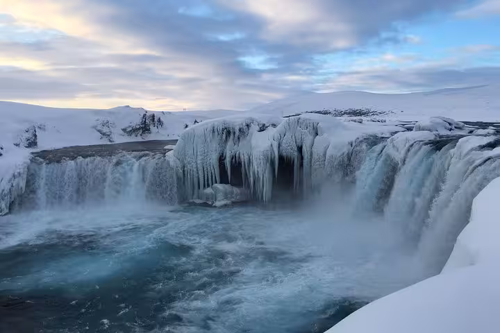 Breathtaking winter scene of a frozen Godafoss Waterfall under a cloudy sky on the Lake Myvatn day tour from Akureyri.