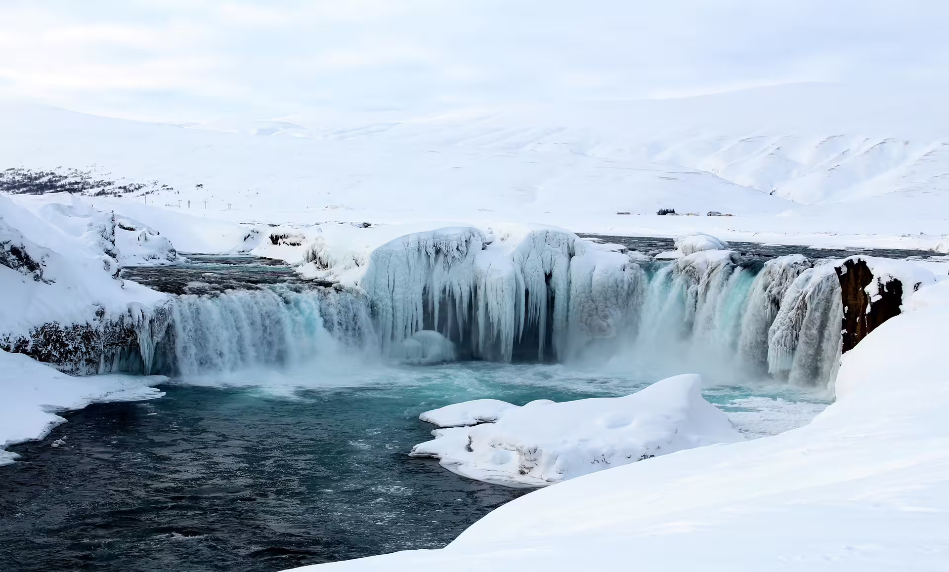 Godafoss waterfall partially frozen with icicles and turquoise water surrounded by snow-covered landscape in Iceland