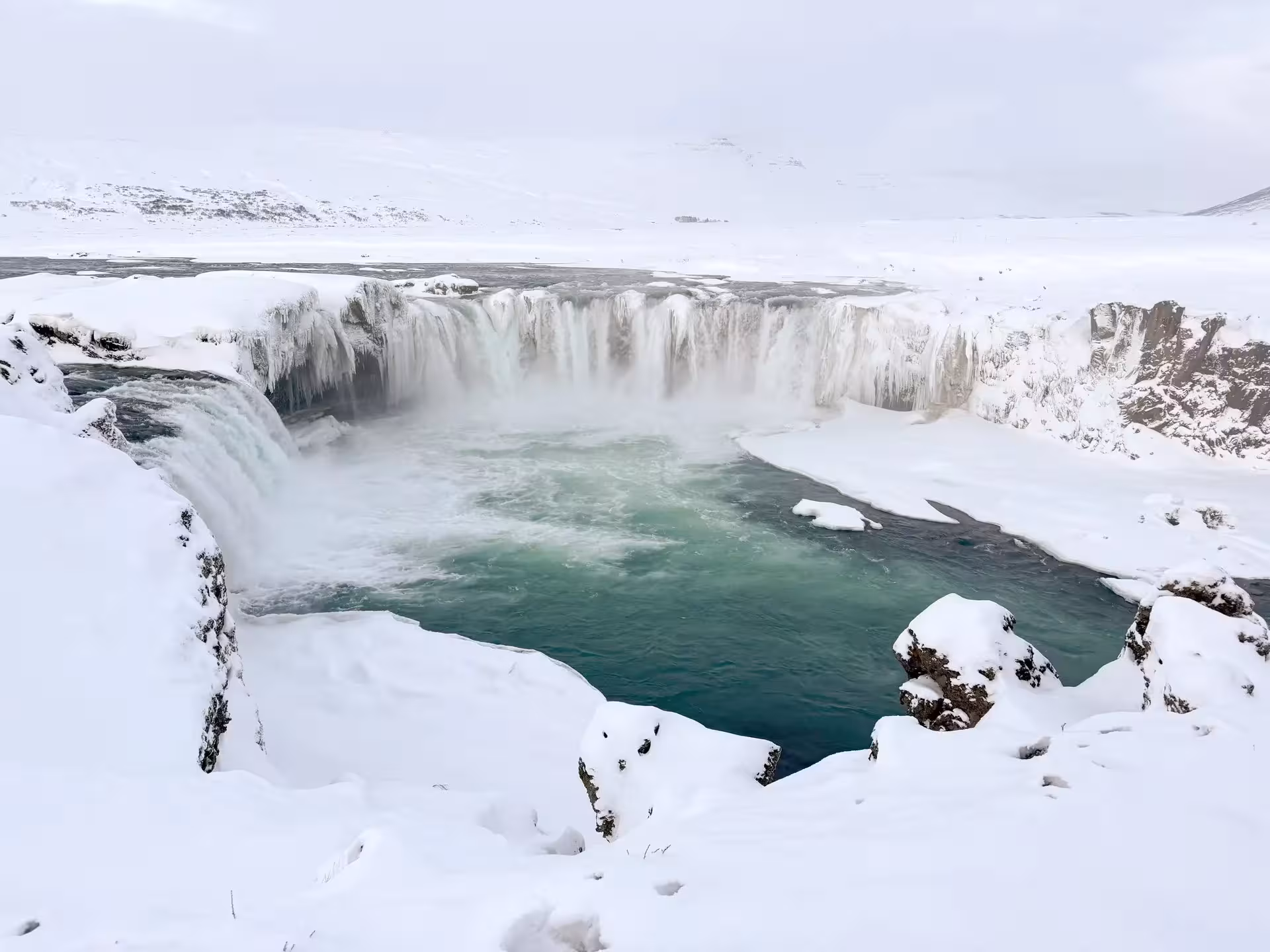 Snowy Goðafoss Waterfall panorama, frozen cliffs and teal pool on Sacred Iceland Christmas Dreams tour