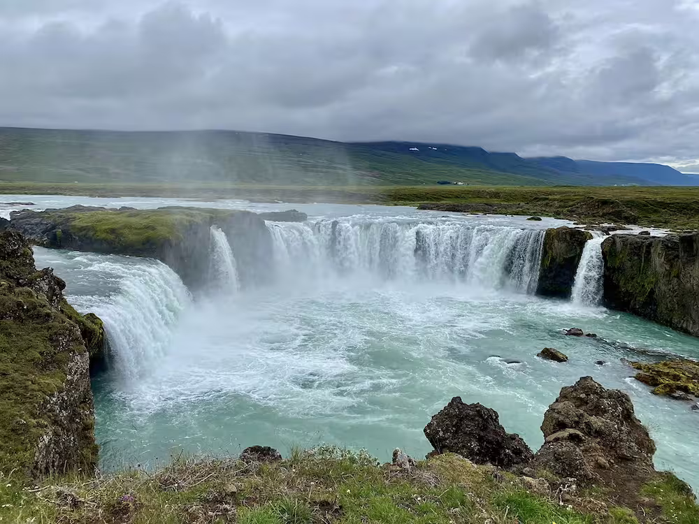 Godafoss waterfall with turquoise waters and misty spray surrounded by green Iceland landscape