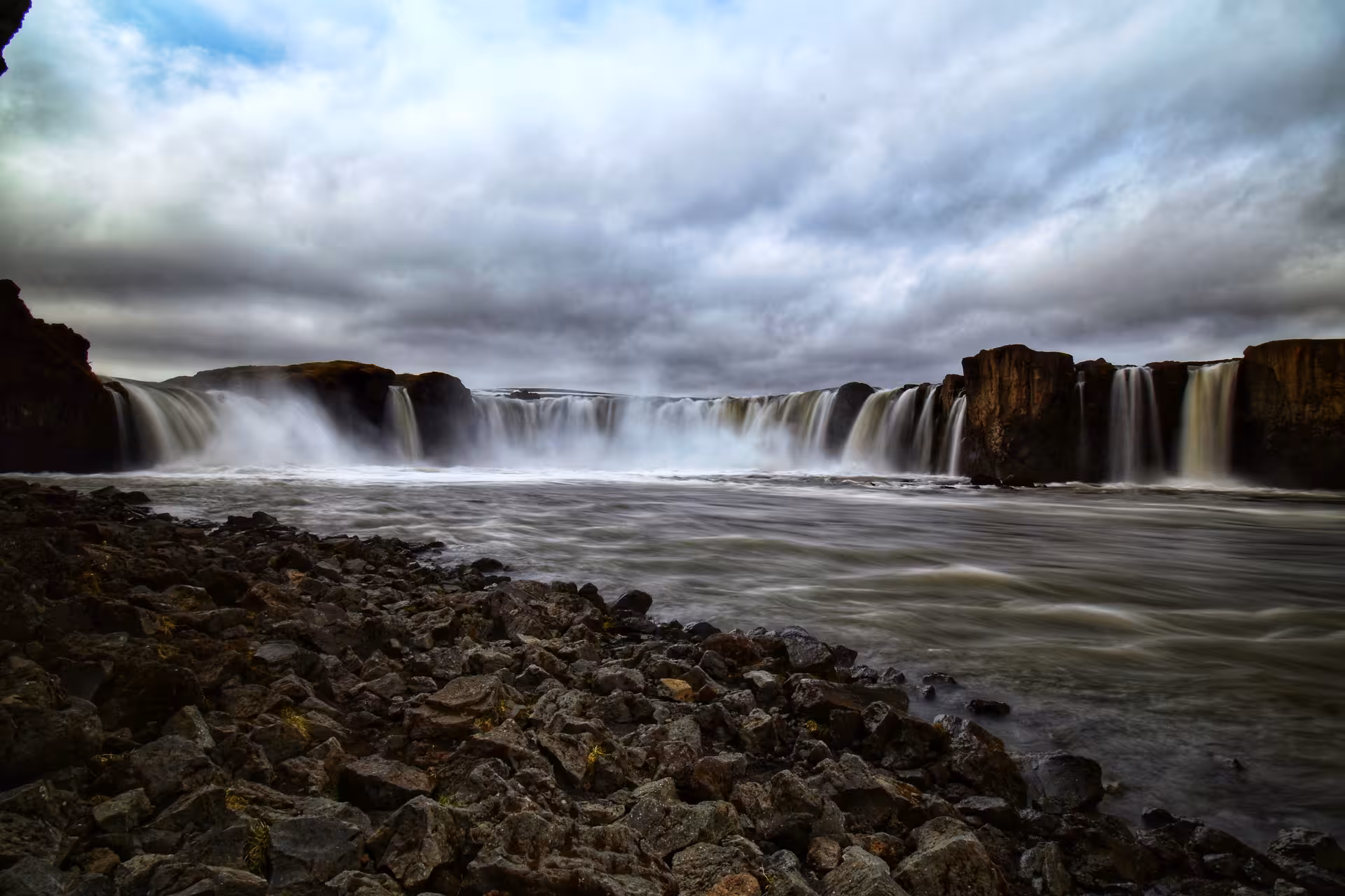 Panoramic view of Godafoss waterfall cascading over basalt cliffs into a misty river in Iceland