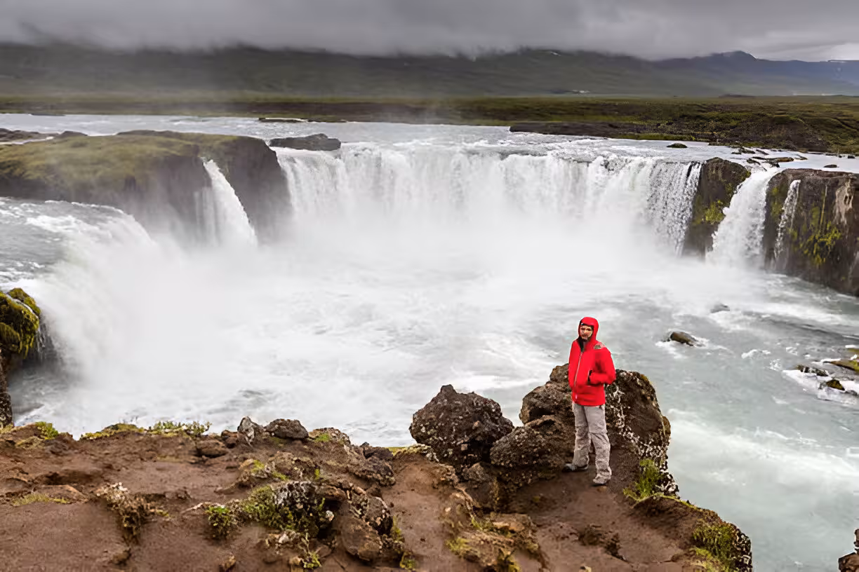Traveler in red jacket standing at the edge of Godafoss waterfall near Lake Myvatn, Iceland