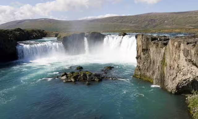 Godafoss waterfall with turquoise waters and rocky cliffs under blue sky in Iceland