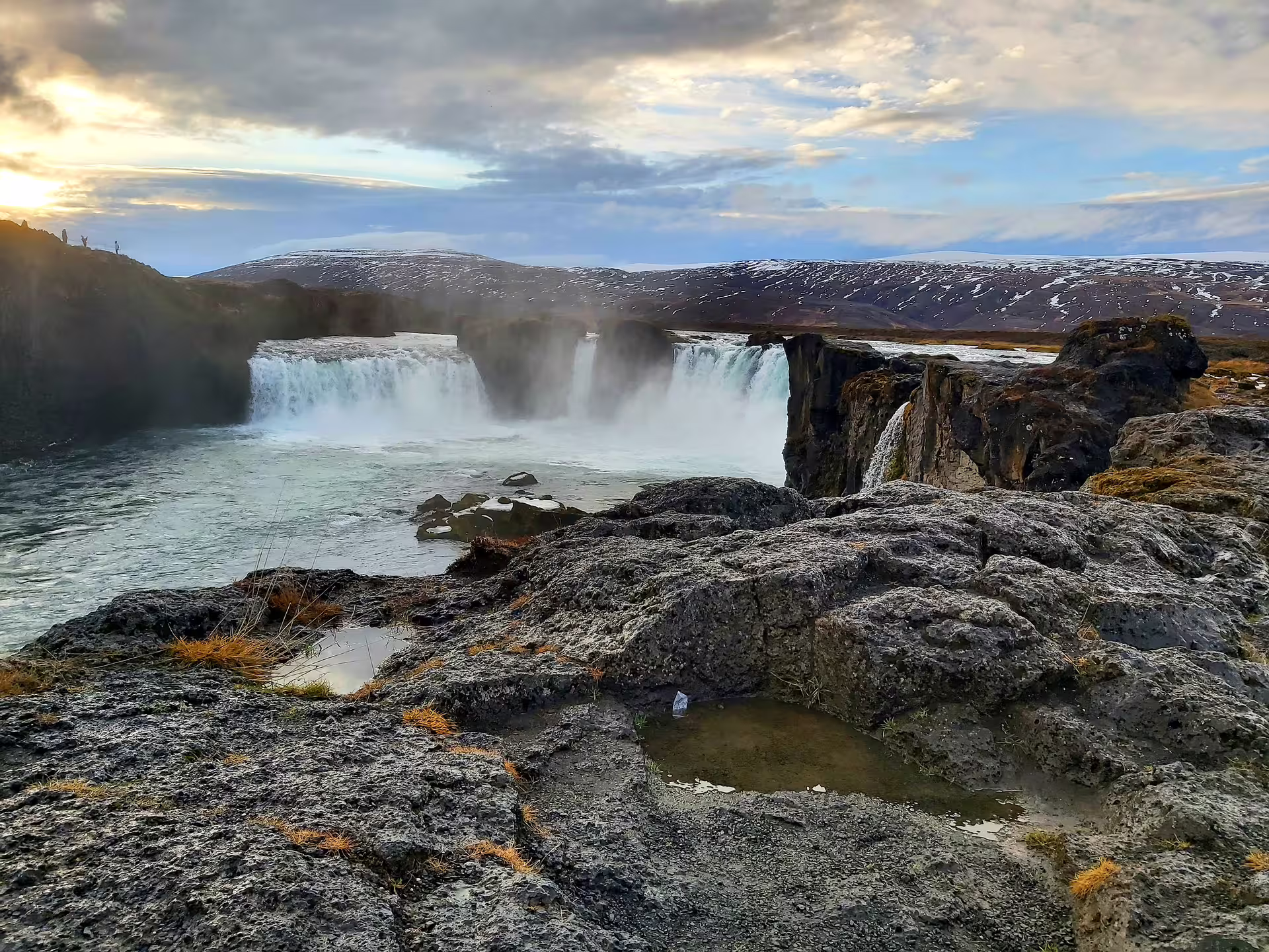 Godafoss waterfall cascading over basalt rocks with misty spray and snow-dusted hills in Iceland