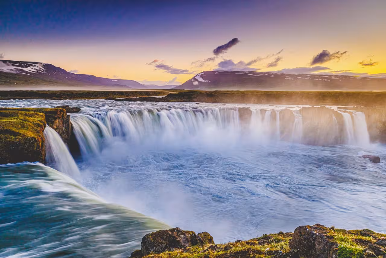 Godafoss waterfall cascading at sunset with snow-capped mountains in background, Diamond Circle Iceland