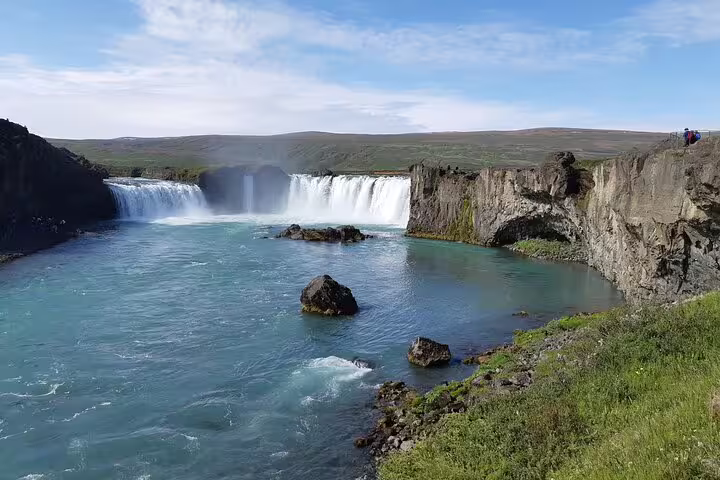 Godafoss waterfall with turquoise glacial waters and rocky cliffs under blue sky, North Iceland