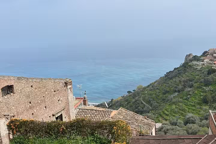 Scenic coastal view from a historic Sicilian village, showcasing rustic buildings and lush greenery overlooking the sea.