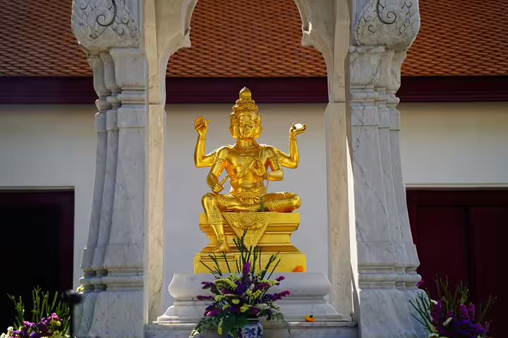 Golden four-armed Brahma statue at a Bangkok temple with marble columns and flower offerings