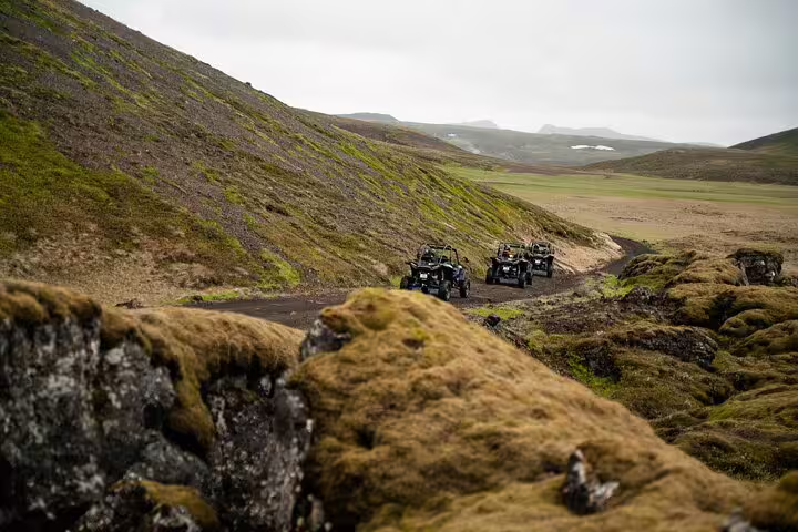 Group of buggy vehicles driving on a winding dirt trail through Iceland's mossy volcanic highlands