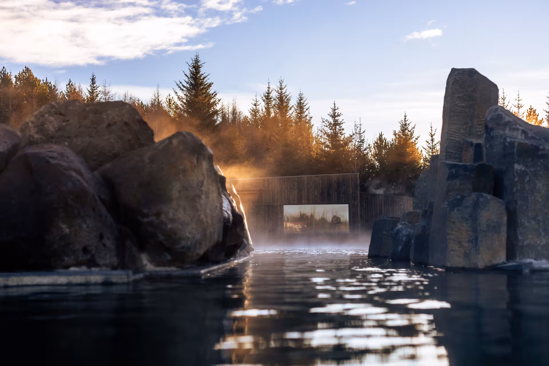 Steaming geothermal lagoon surrounded by volcanic rocks and pine trees at golden hour in Iceland