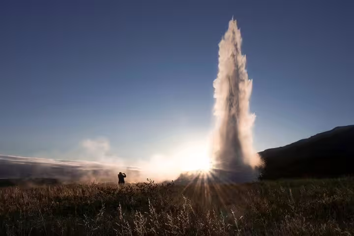 Geyser erupting at sunset on the Golden Circle tour in Iceland with a lone visitor silhouetted nearby
