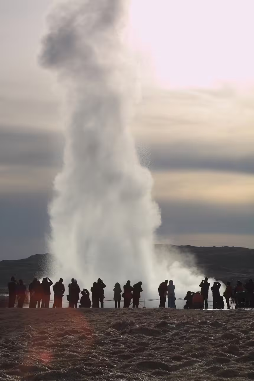 Tourists silhouetted watching Strokkur geyser eruption on Iceland's Golden Circle tour at dusk