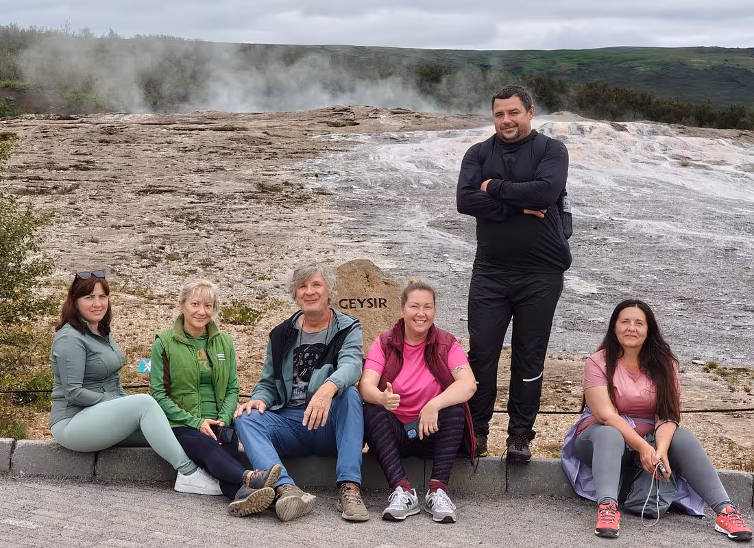 Group of tourists posing at Geysir sign with steaming hot spring on Iceland's Golden Circle tour