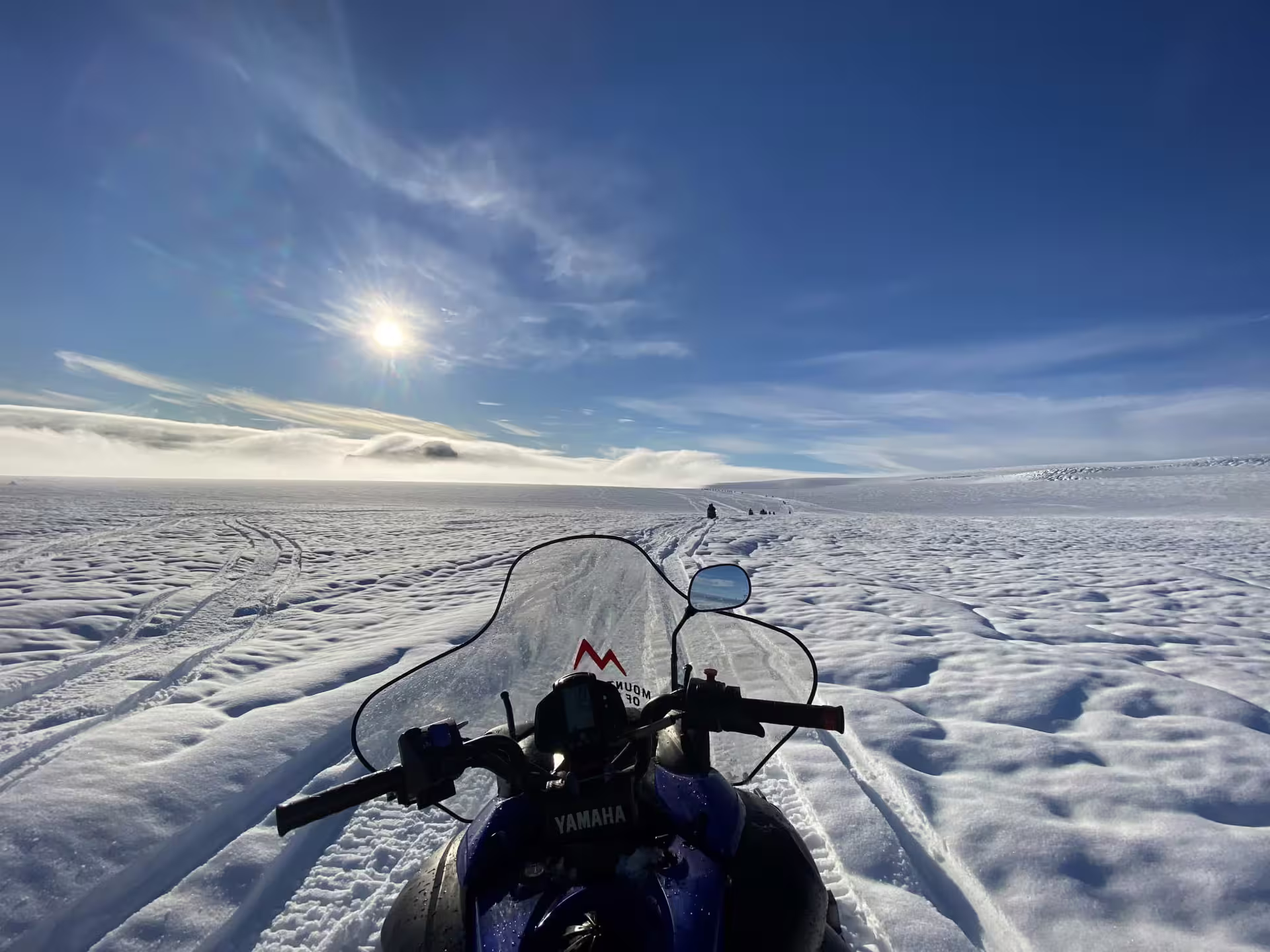 Rider's POV on a Yamaha snowmobile crossing Iceland's vast glacier under a bright sunny blue sky on a Golden Circle tour