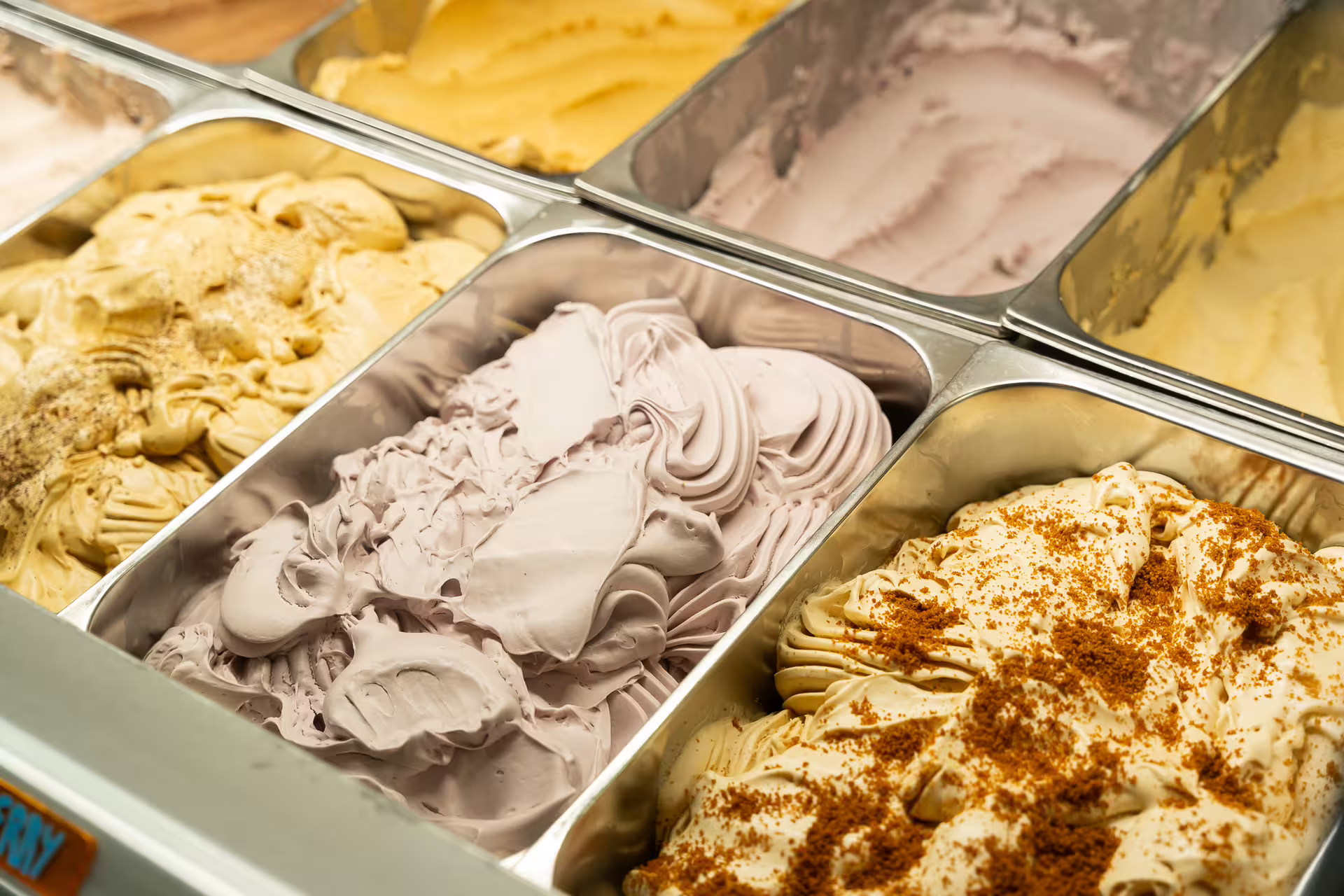 Assorted gelato flavors in stainless steel trays at a gourmet ice cream display