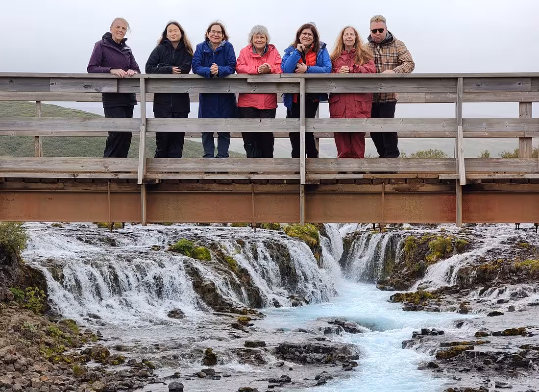 Group of seven tourists on wooden bridge over Bruarfoss waterfall with turquoise water, Iceland Golden Circle