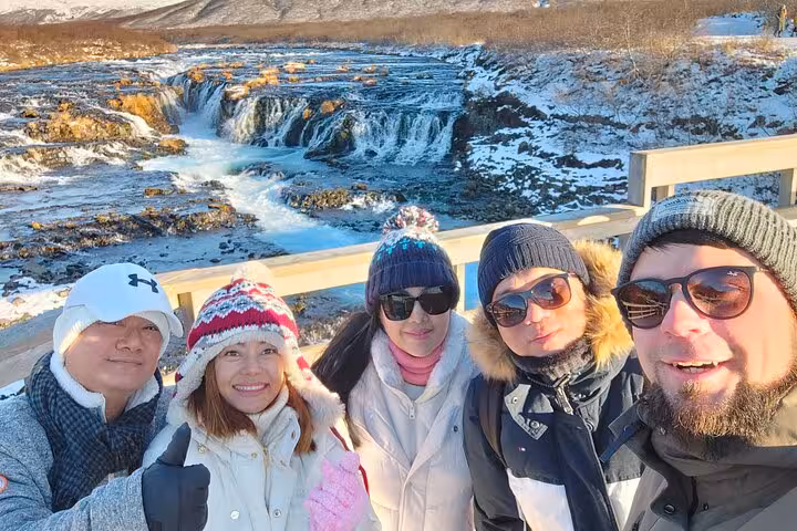 Group of five tourists taking selfie at Bruarfoss waterfall on Golden Circle tour in winter Iceland