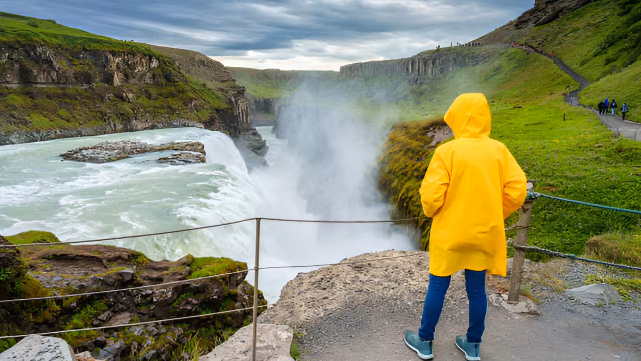 Traveler in yellow raincoat overlooking Gullfoss waterfall canyon on Iceland Golden Circle tour