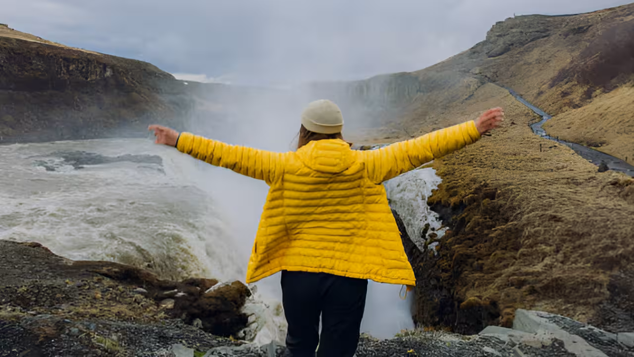 Traveler in yellow jacket arms outstretched at Gullfoss waterfall on Golden Circle Iceland