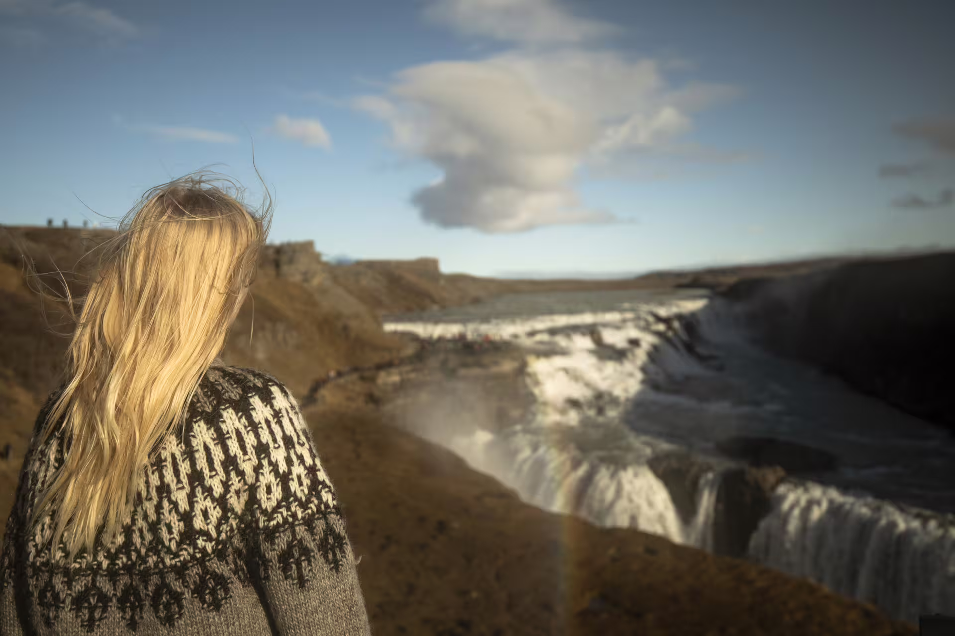 Blonde woman in Icelandic lopapeysa sweater overlooking Gullfoss waterfall on Golden Circle tour
