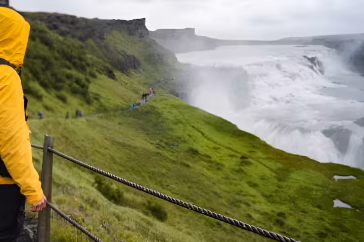 Hiker in yellow rain jacket overlooking Gullfoss waterfall on Iceland's Golden Circle tour