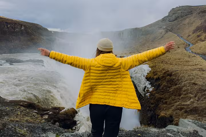 Traveler in yellow jacket spreading arms at Gullfoss waterfall on Iceland Golden Circle tour