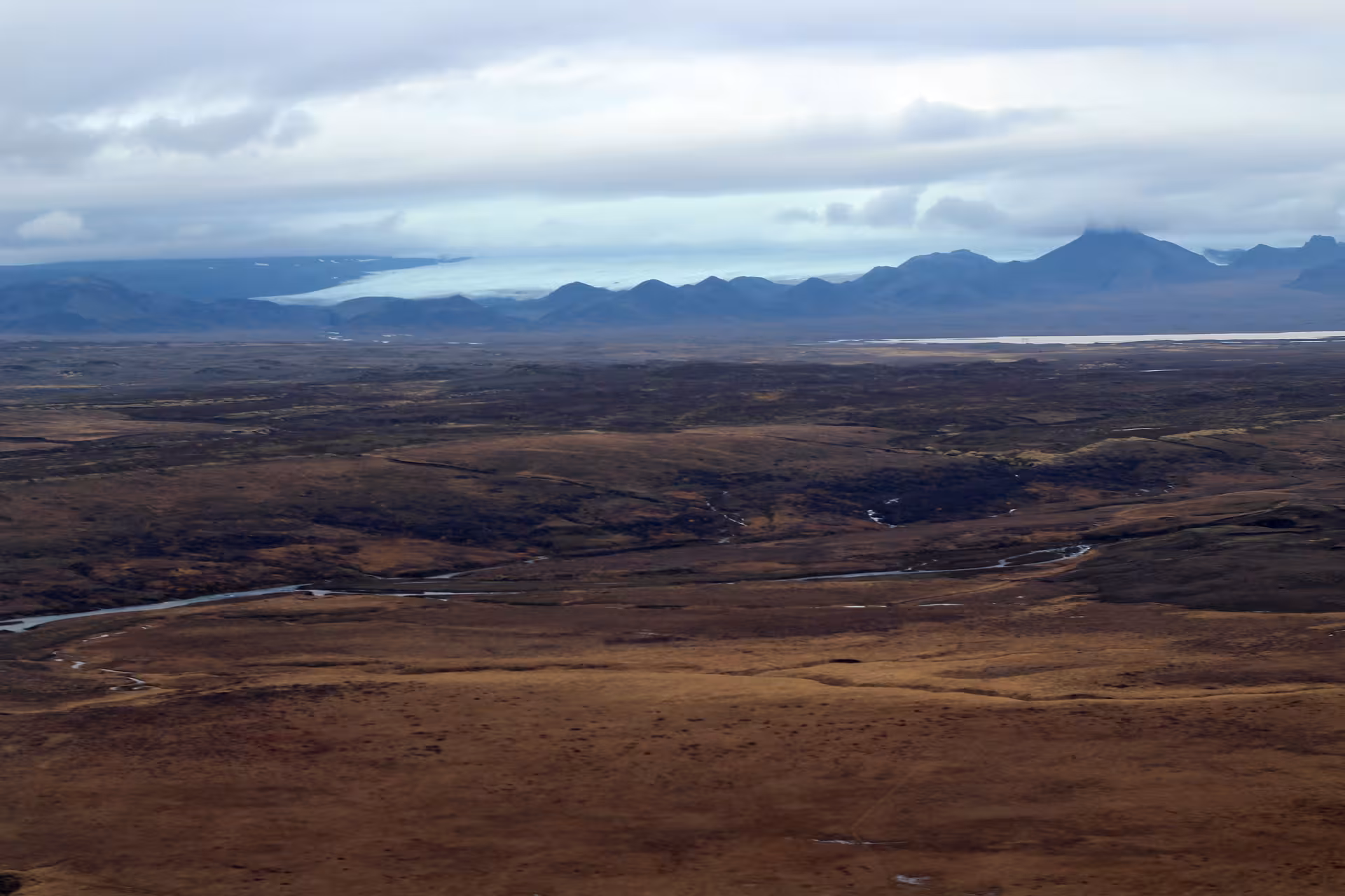 Aerial view of Iceland's vast golden tundra plains with winding rivers and distant mountains from airplane tour