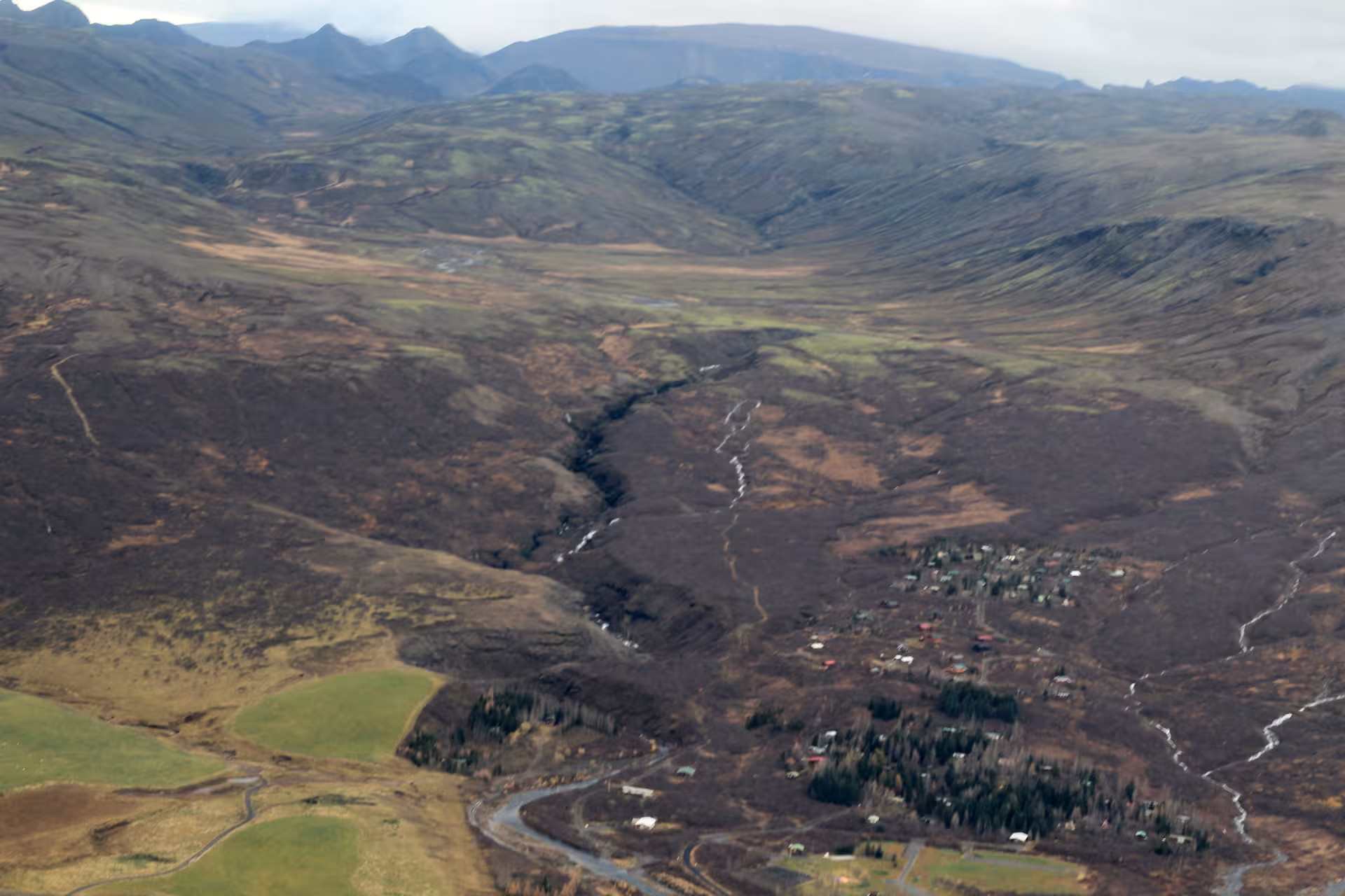 Aerial view of Icelandic valley with small town, winding river, and volcanic landscape from airplane