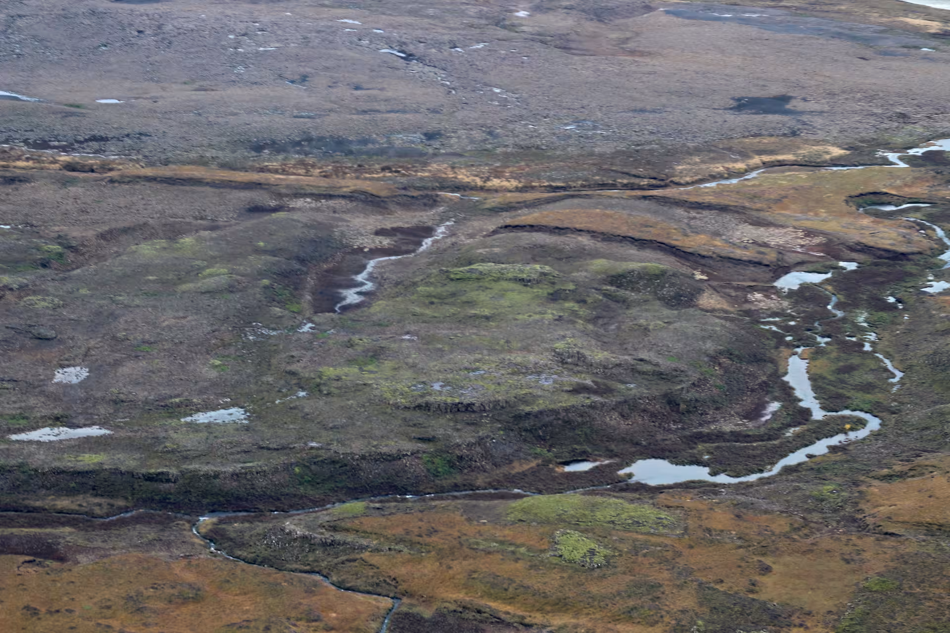 Aerial view of Icelandic tundra wetlands with winding streams and patches of snow from airplane
