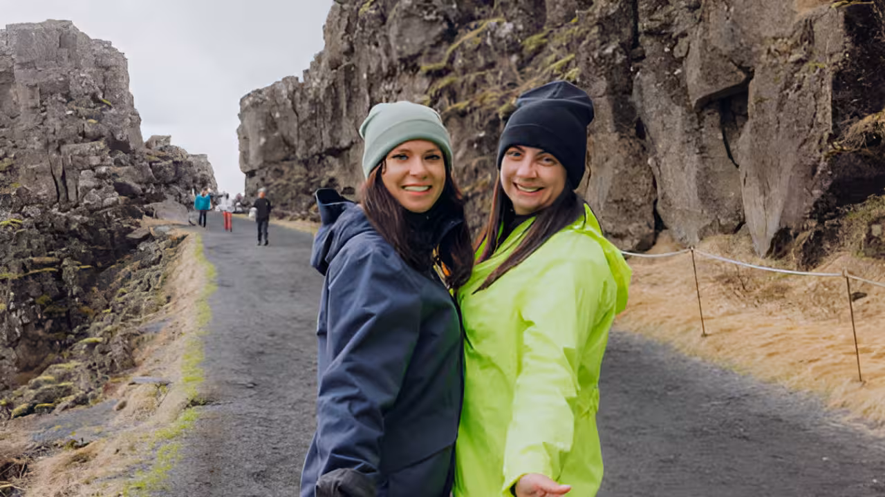 Two smiling women in winter jackets and beanies on a rocky canyon path in Iceland's Golden Circle