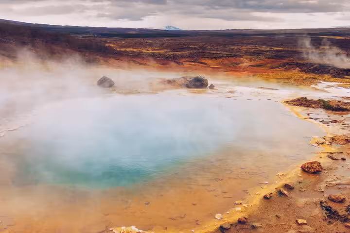 Steaming turquoise geothermal hot spring pool with colorful mineral deposits in Iceland