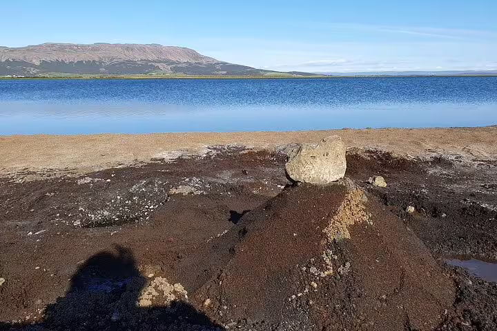 Rocky lakeshore with calm blue lake and volcanic mountain in Iceland on a clear day