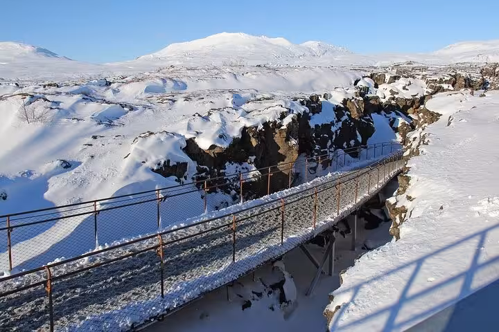 Snow-covered bridge over rocky fissure in Icelandic winter landscape with mountain backdrop