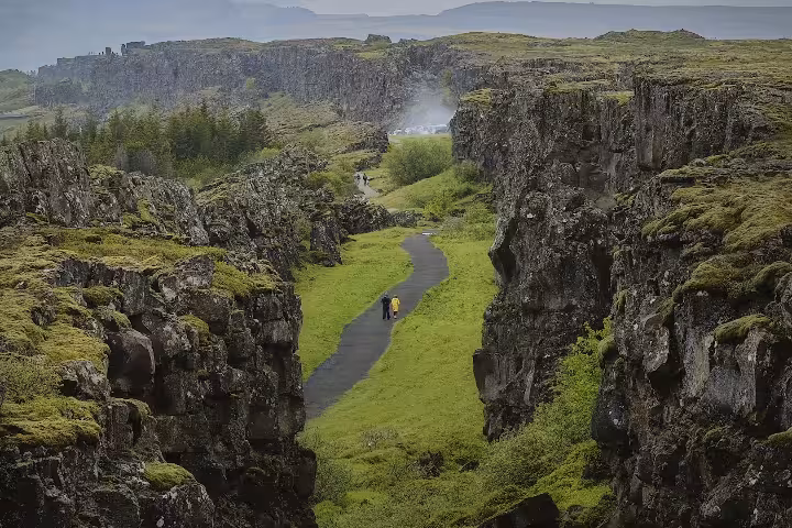 Two hikers walking through a dramatic rocky canyon with lush green moss at Þingvellir, Iceland
