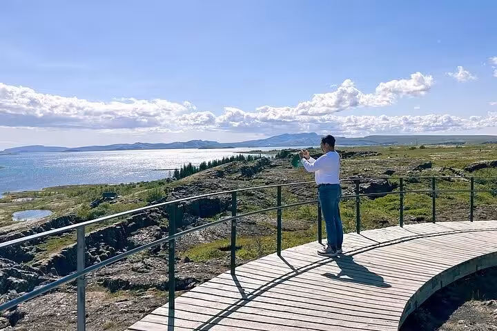 Tourist photographing Þingvellir lake landscape on wooden viewpoint boardwalk, Golden Circle Iceland