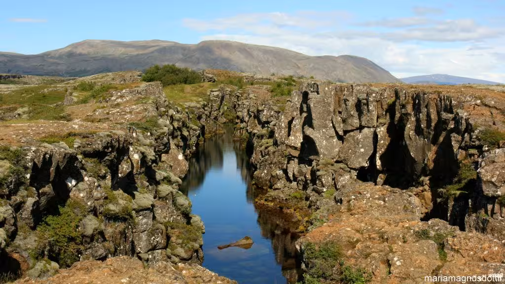 Rocky lava fissure with calm water channel at Þingvellir National Park, Iceland, mountains in background