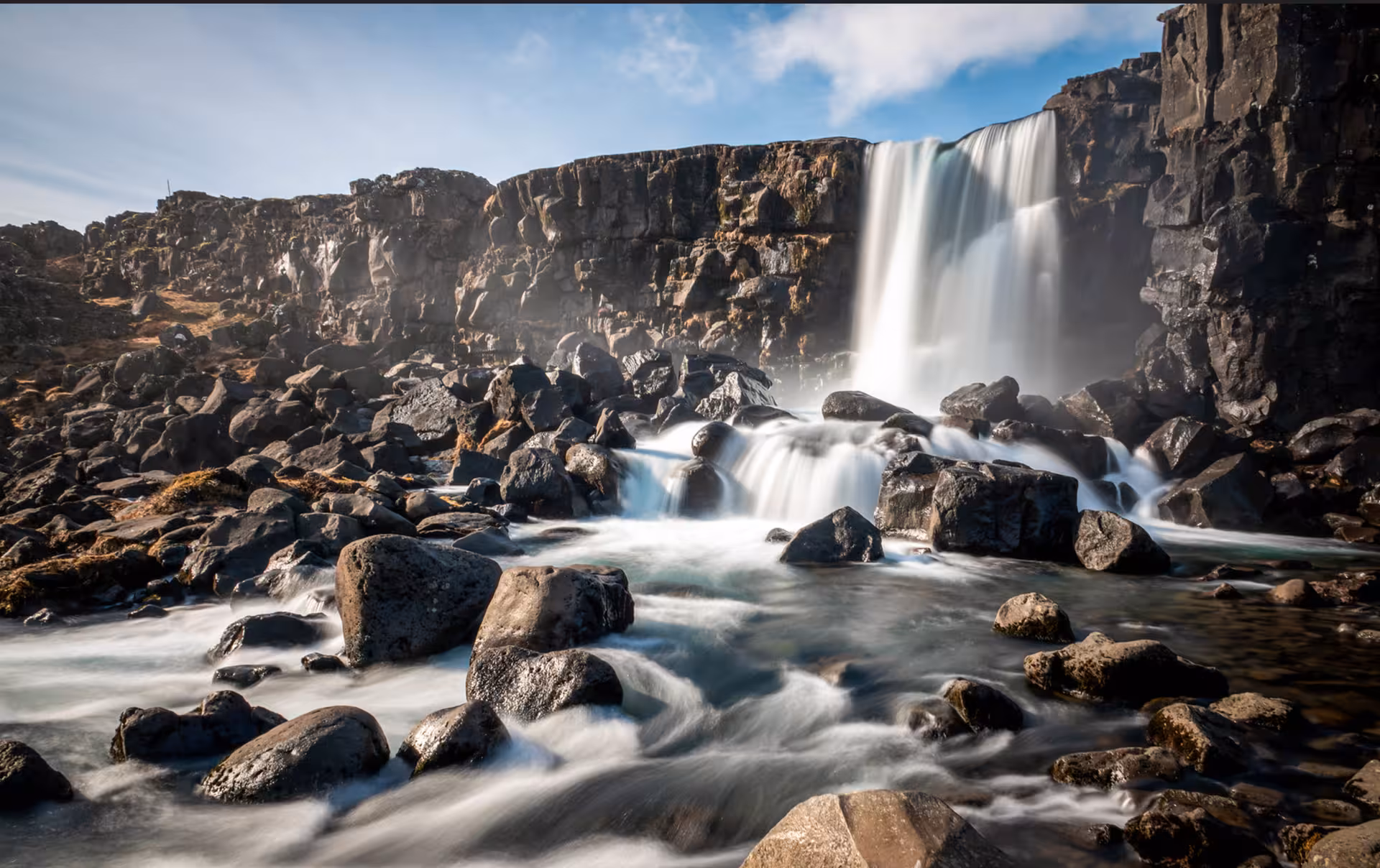 Öxará waterfall cascading over dark basalt cliffs into rocky stream at Þingvellir, Golden Circle Iceland