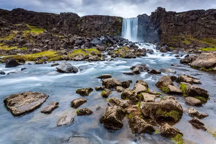Öxará river flowing over mossy rocks with Öxarárfoss waterfall in Þingvellir, Iceland