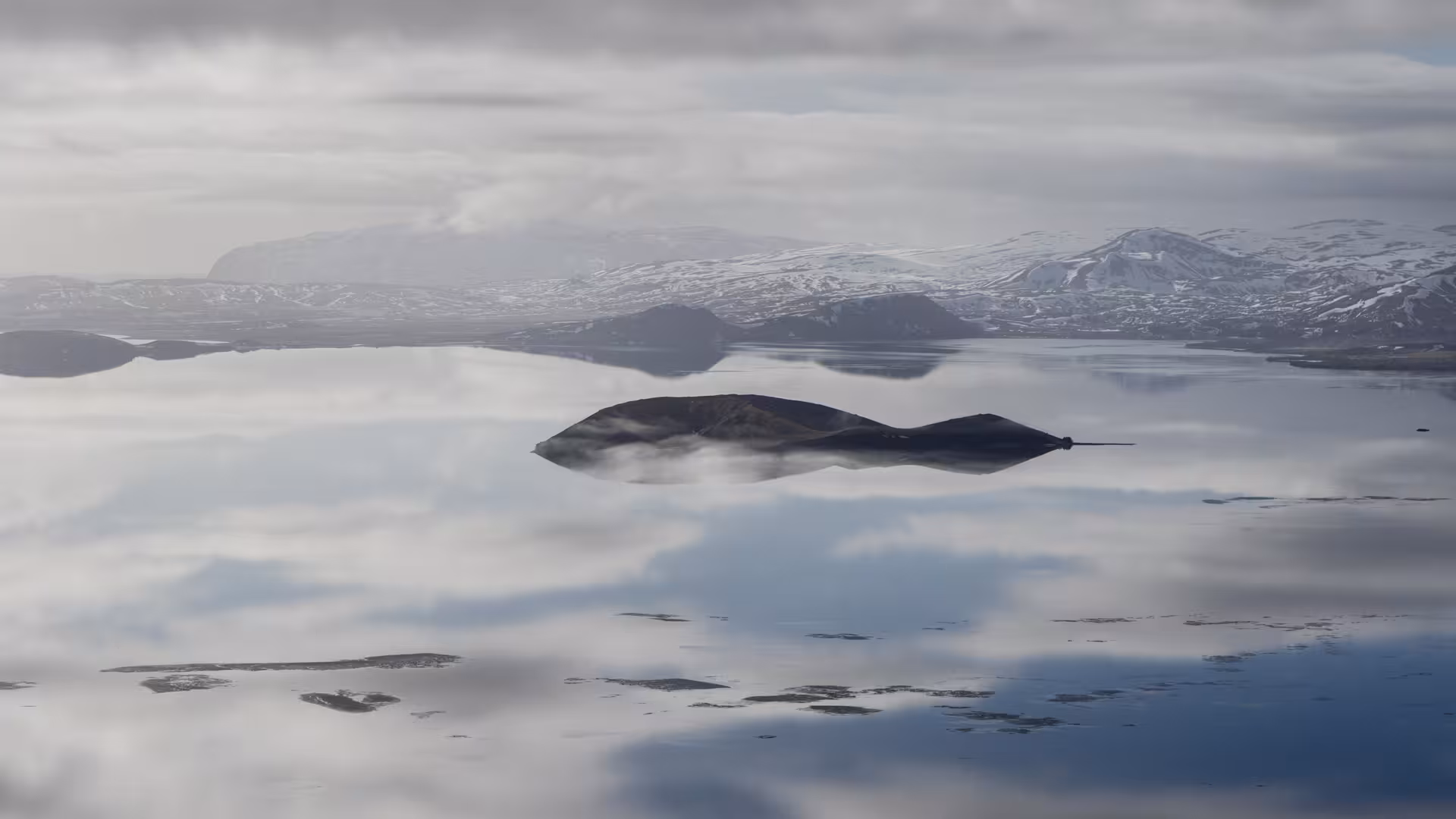 Aerial view of volcanic island reflected in still water with snow-capped mountains in Iceland