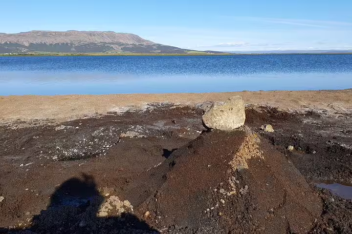Rocky lakeshore with calm blue lake and mountain backdrop near Reykjavik Golden Circle