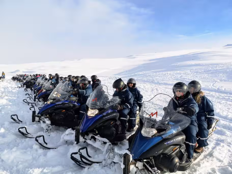 Group of travelers on snowmobiles lined up on Iceland glacier during an adventurous Golden Circle snowmobile tour