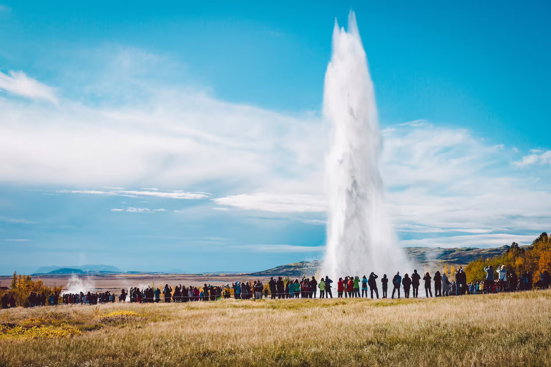Crowds watching Strokkur geyser erupt on Iceland's Golden Circle tour under blue skies