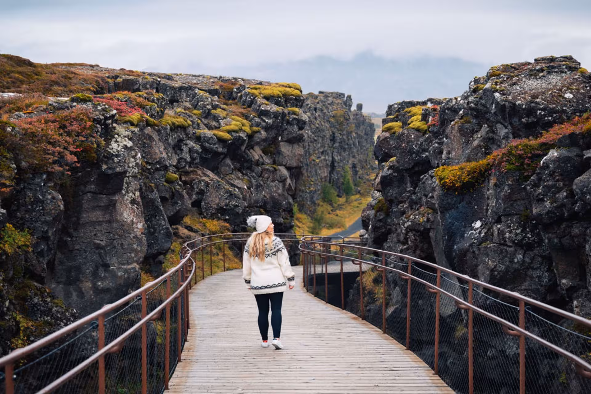 Woman in Nordic sweater walking wooden boardwalk through Þingvellir tectonic rift canyon, Iceland