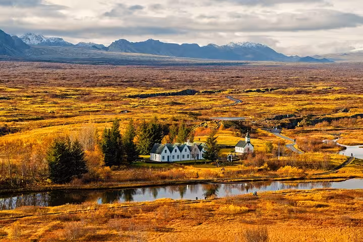 Aerial view of Þingvellir National Park in autumn with white church, river, and snow-capped mountains, Iceland